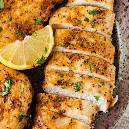 Air Fryer Chicken Breast on serving plate sliced with lemon wedges and parsley garnish