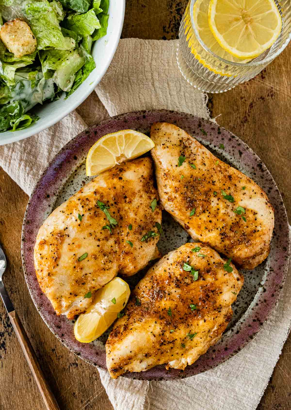 Air Fryer Chicken Breast on serving plate with lemon wedges and parsley garnish