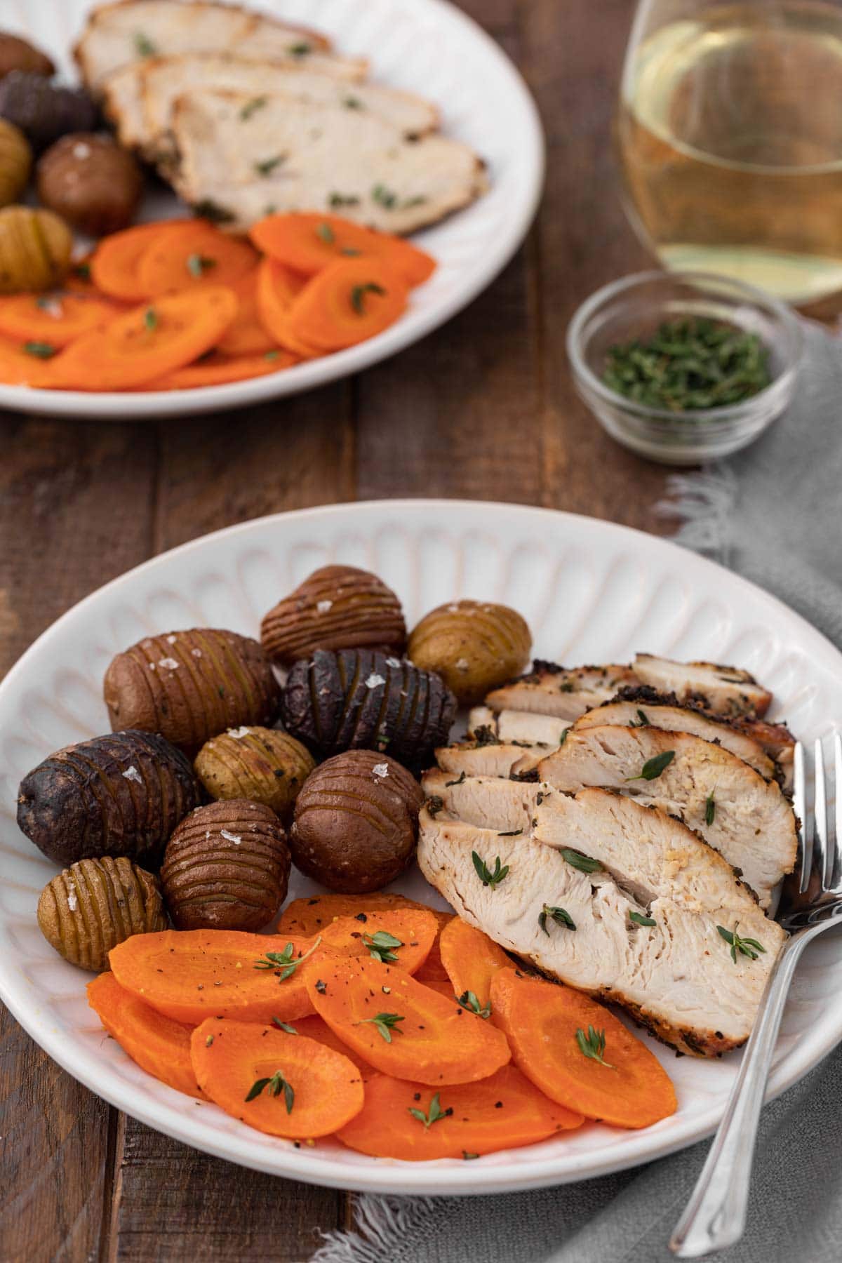 Air Fryer Herb Butter Turkey Breast two plates of sliced cooked turkey with carrots and mini hasselback potatoes, glass of white wine to right