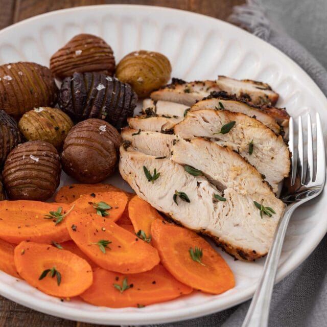Air Fryer Herb Butter Turkey Breast sliced cooked turkey plated with carrots and mini hasselback potatoes, with fork on plate, 1x1
