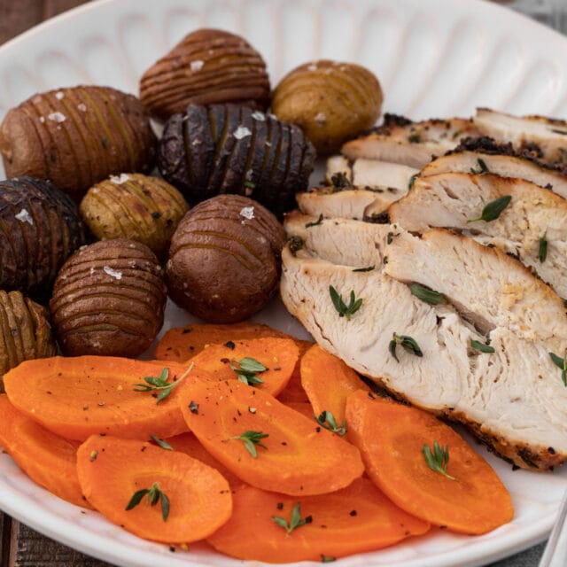sliced cooked turkey plated with carrots and mini hasselback potatoes