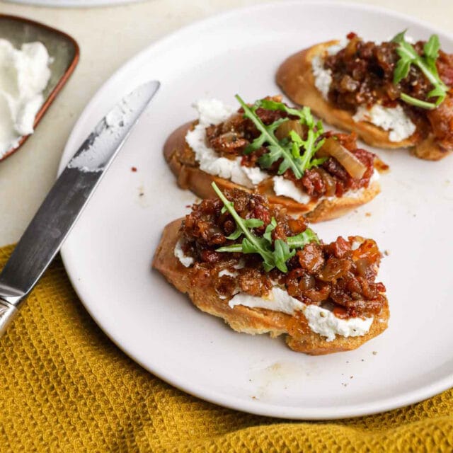 Bacon Jam spread on three baguette slices on plate with butter knife