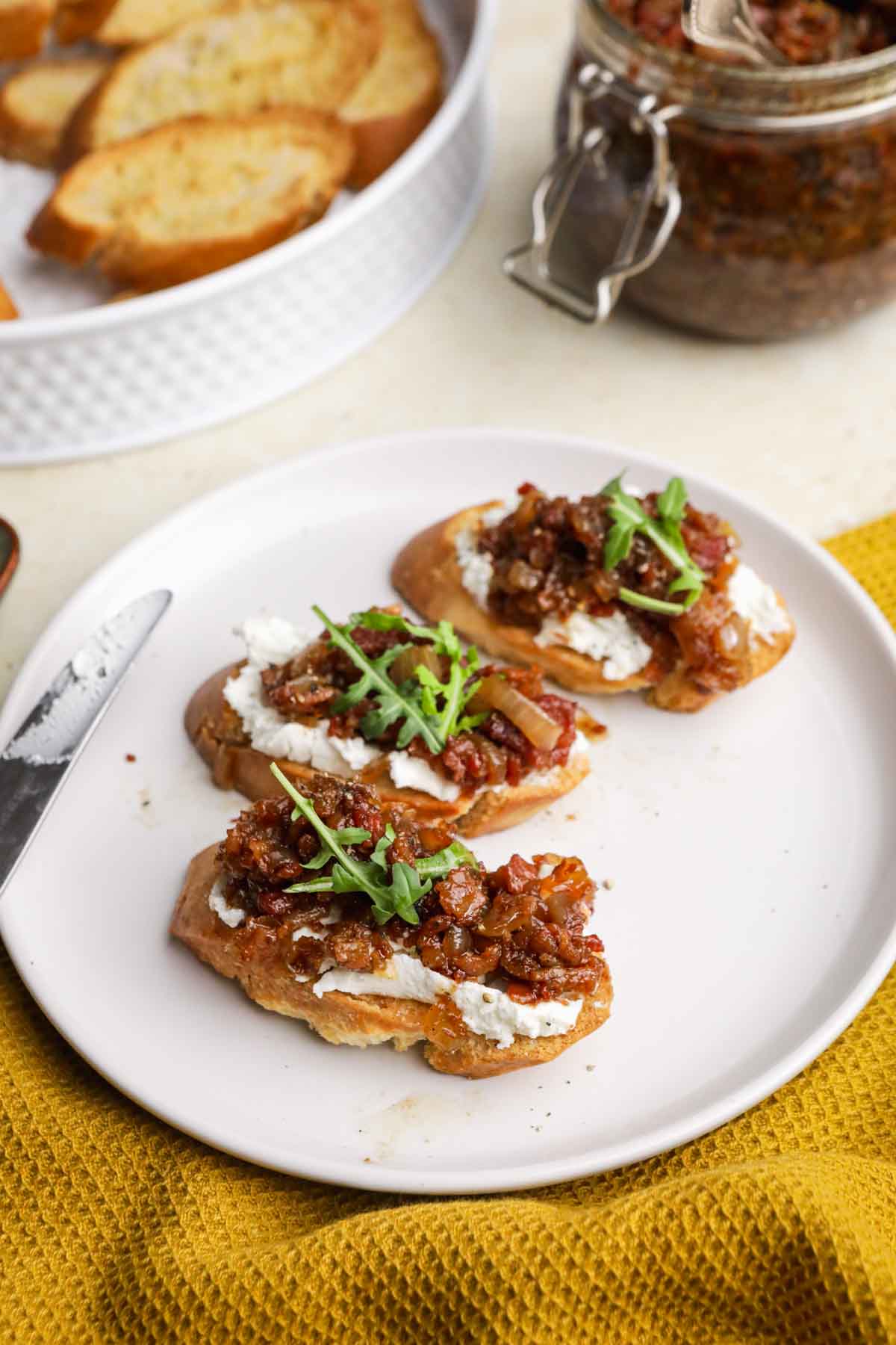 Bacon Jam spread on three baguette slices on plate with butter knife