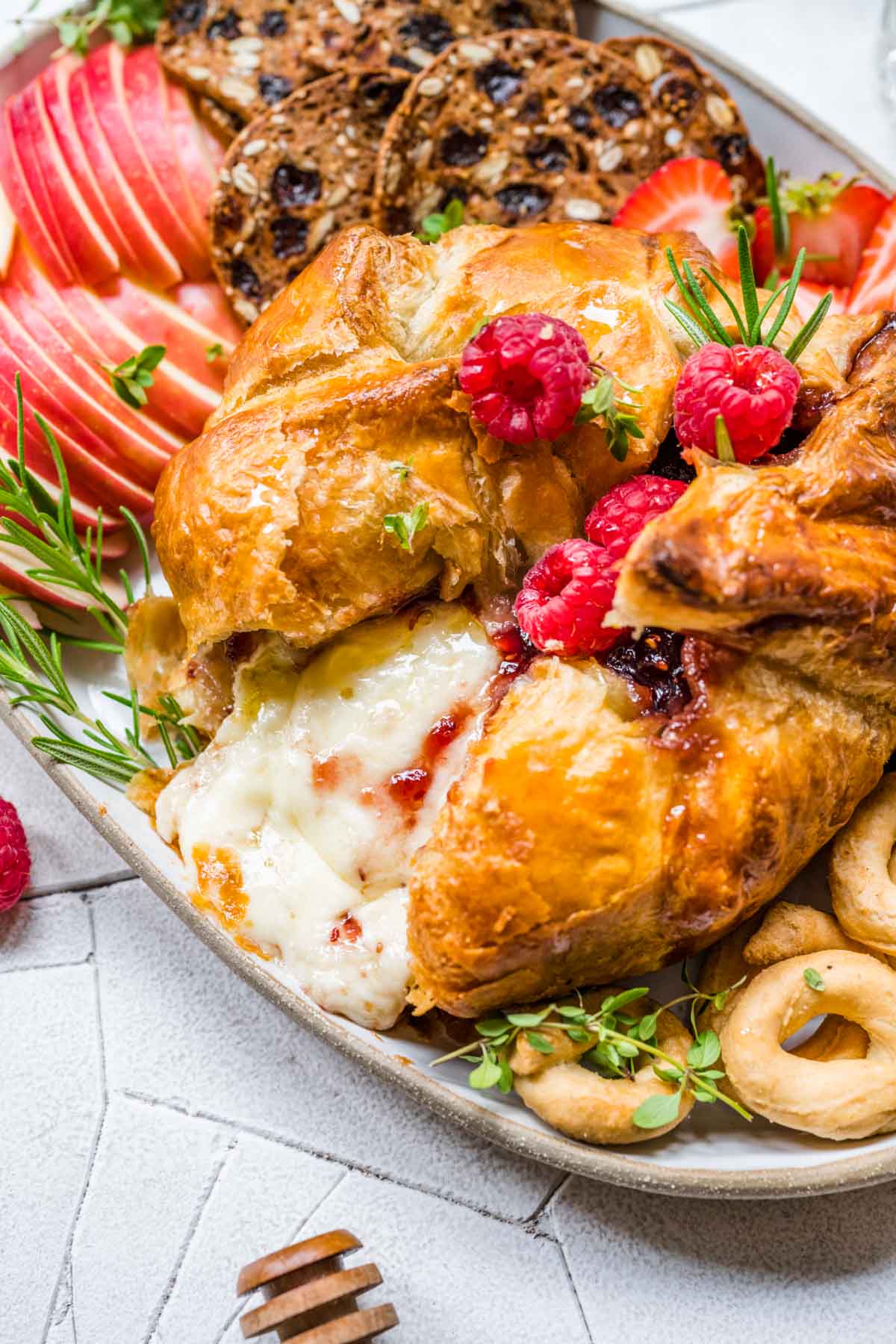 Baked Brie on serving platter with fresh raspberry garnish, apples and crackers, melted cheese showing