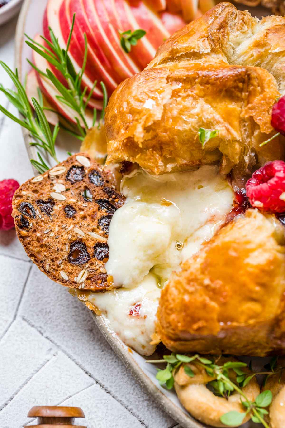 Baked Brie on serving platter with fresh raspberry garnish, apples and crackers, melted cheese showing