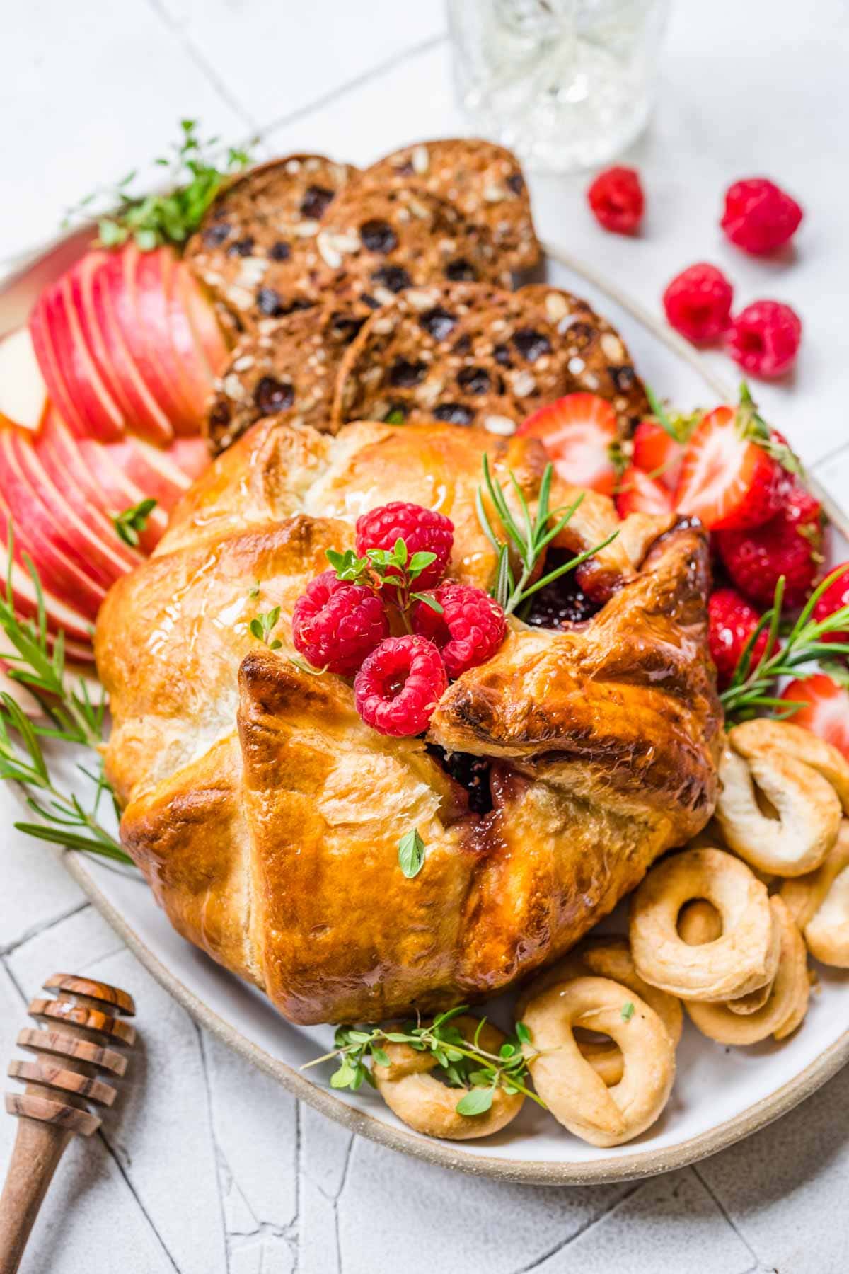 Baked Brie on serving platter with fresh raspberry garnish, apples and crackers