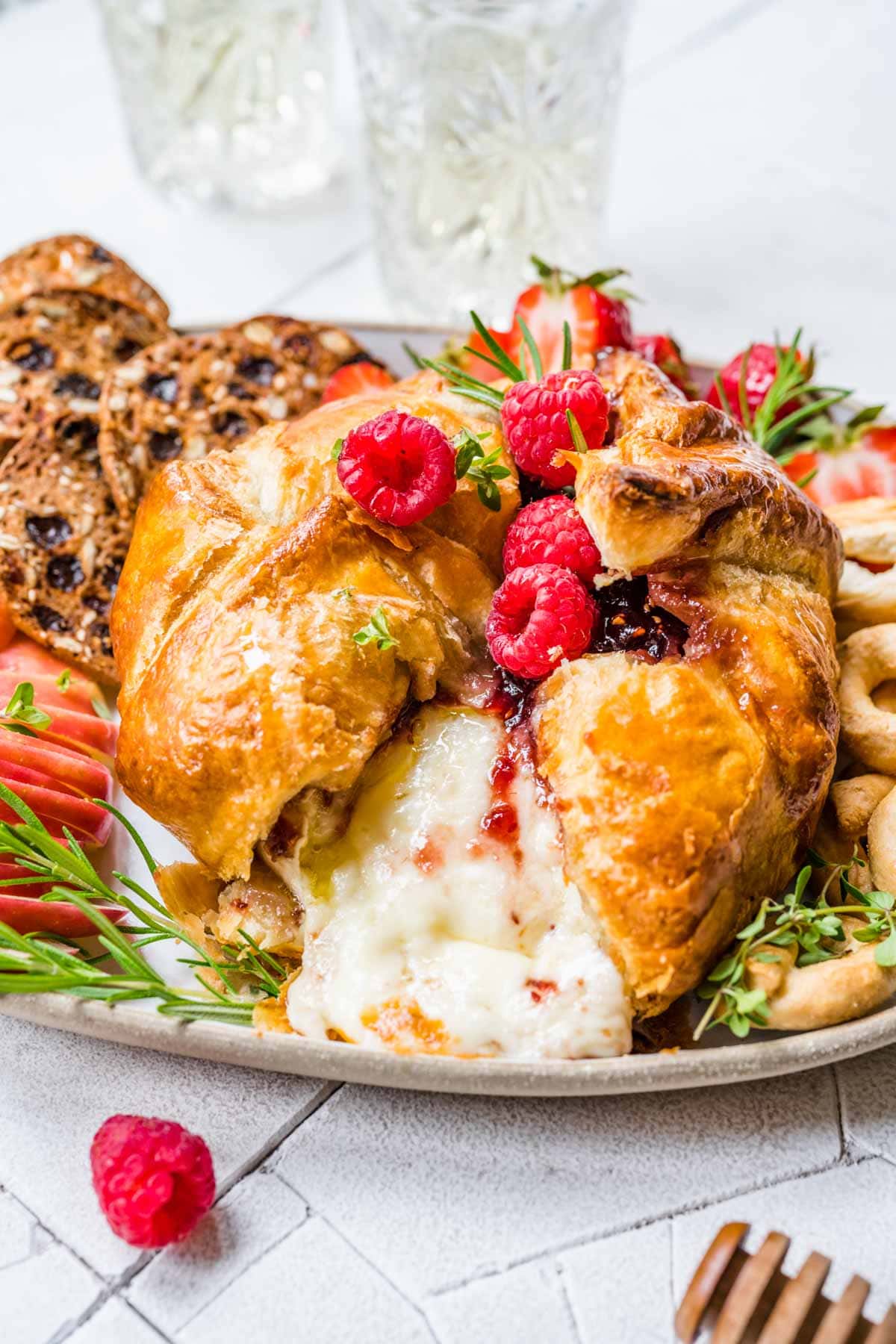 Baked Brie on serving platter with fresh raspberry garnish, apples and crackers, melted cheese showing