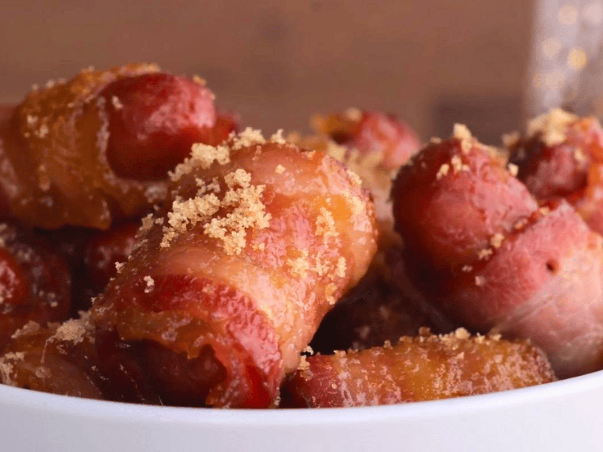 hot dogs wrapped in bacon and brown sugar stacked on one another in a white bowl