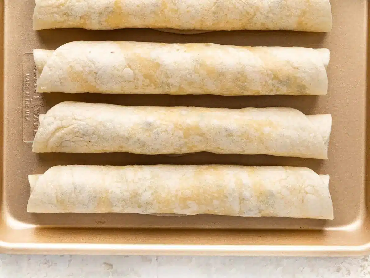 Rolled tortillas with spread inside on a baking sheet