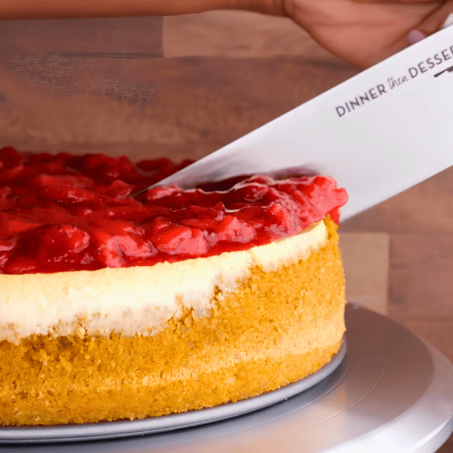 cream cheese dessert with strawberries on a cake platter with a knife cutting into it