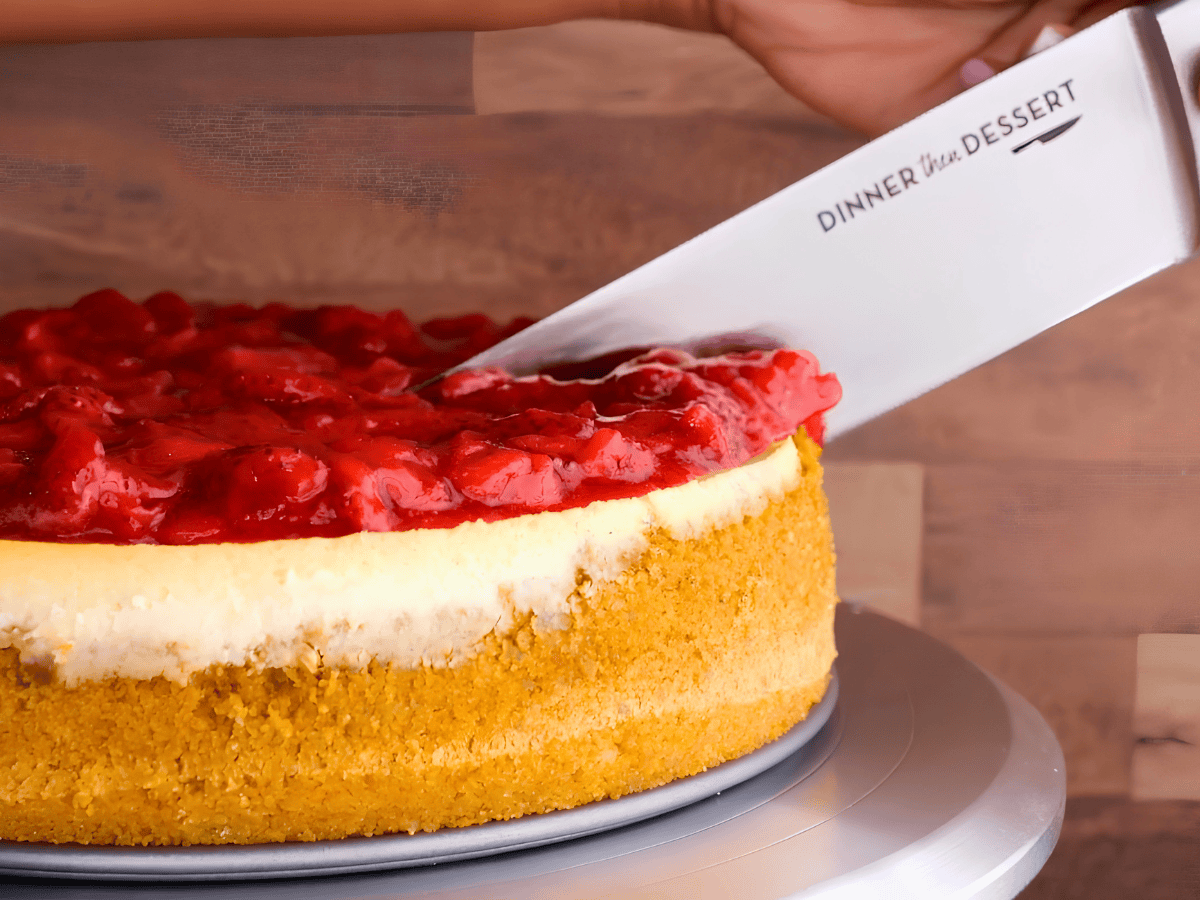 cream cheese dessert with strawberries on a cake platter with a knife cutting into it