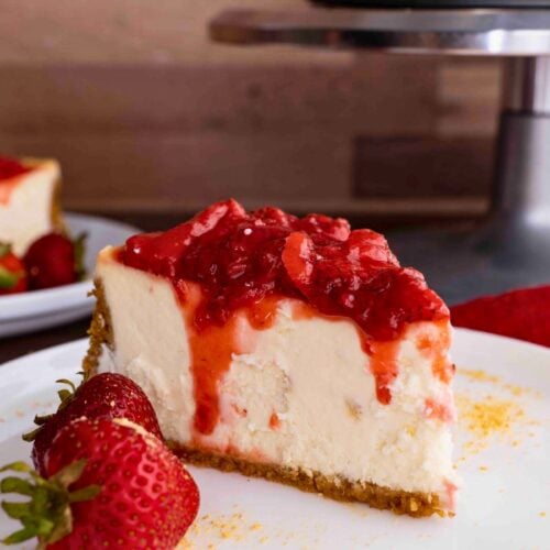 Slice of cheesecake with strawberry topping on plate with berries