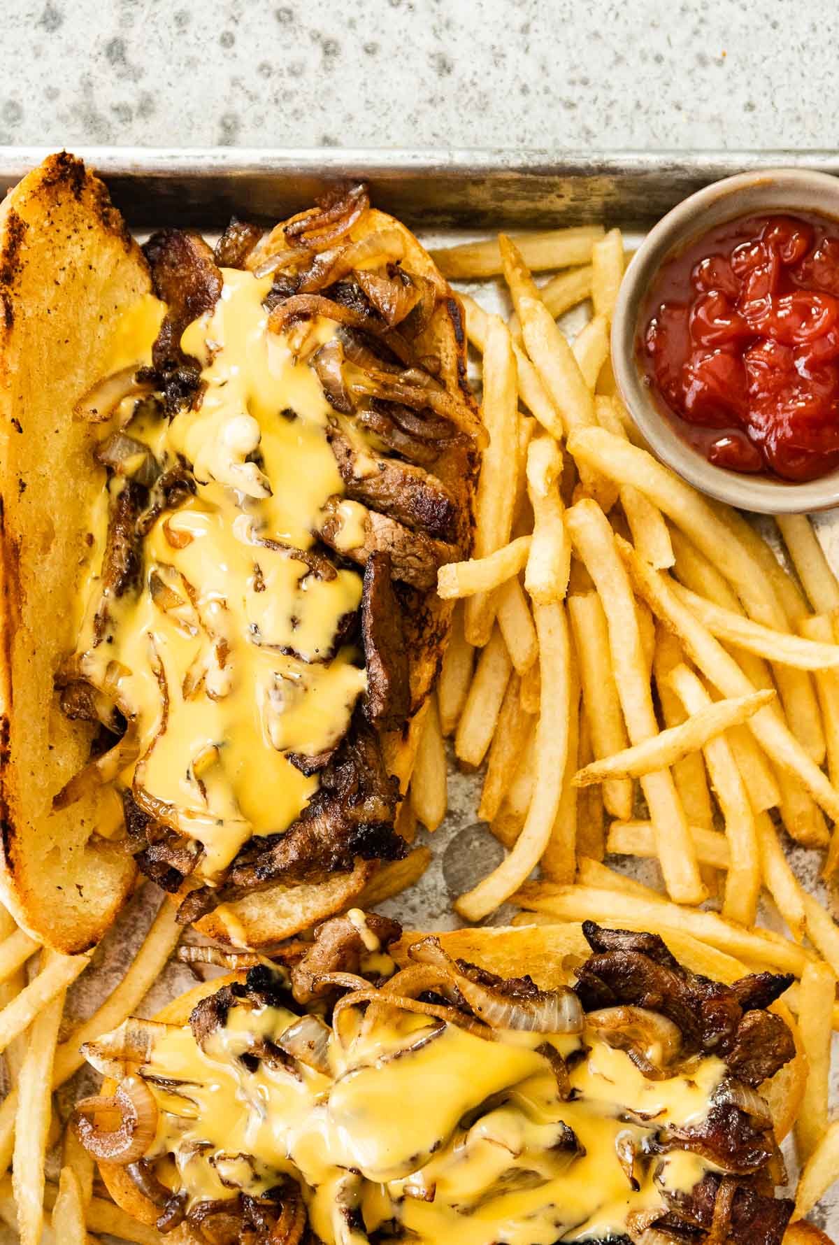 Philly Cheesesteak on serving plate with cheese sauce and fries