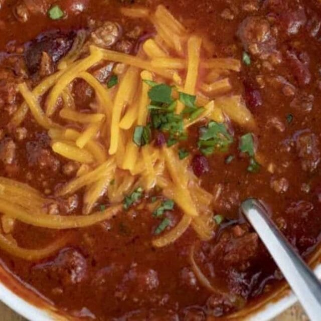 Chili in a white bowl with cheese for garnish.