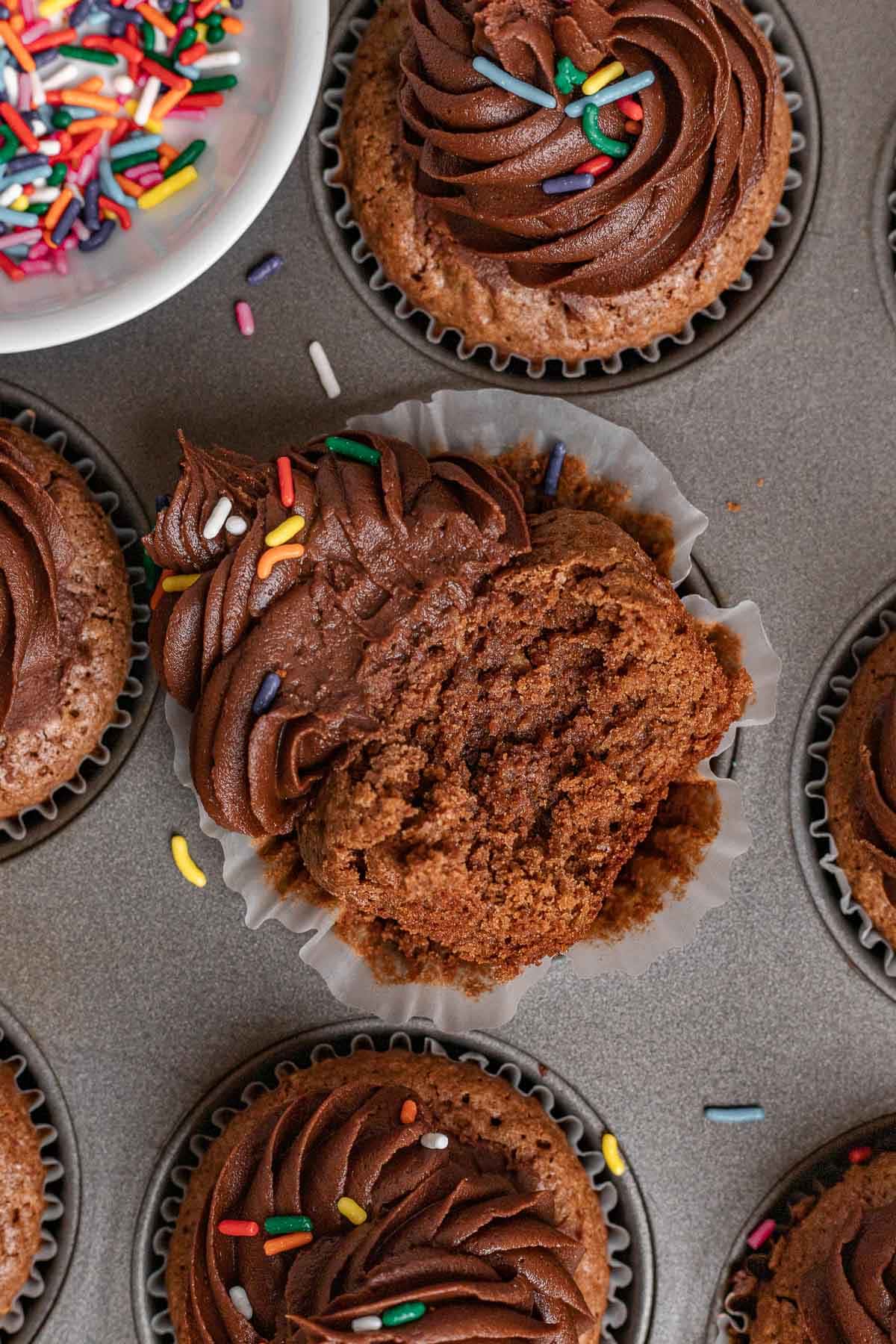Brownie Cupcakes frosted with wrapper partially removed in muffin tin with bite take out