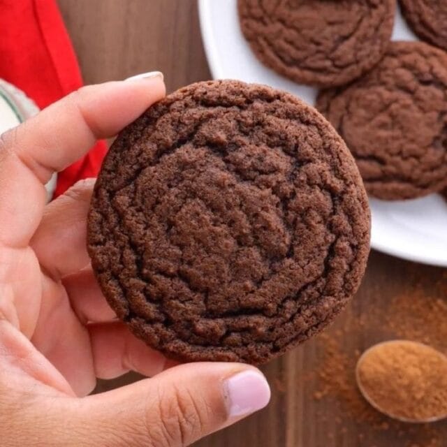 hand holding baked cookie over cookies on plate