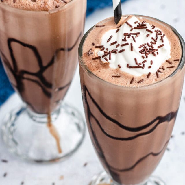 Two milkshakes with whipped cream, sprinkles and straws.