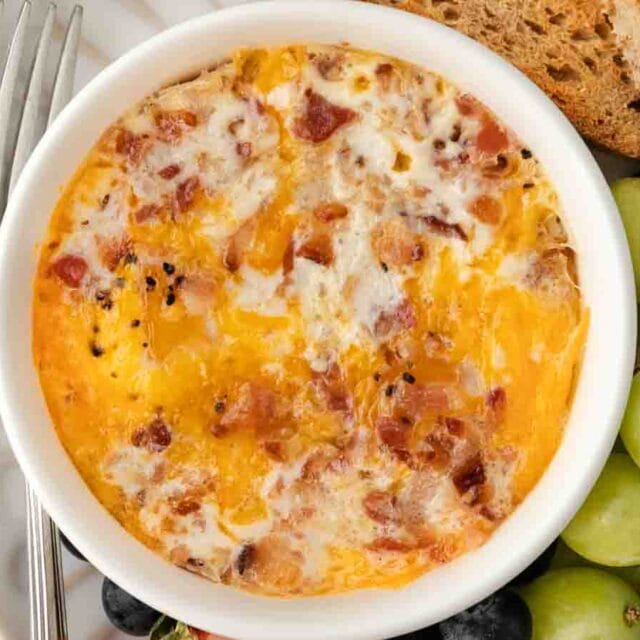 Close up of baked egg in ramekin with cheese and bacon.
