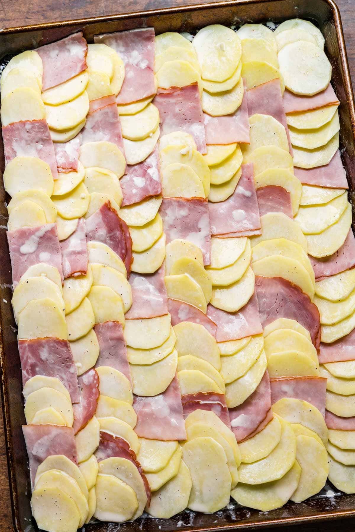 Sheet Pan Ham and Swiss Scalloped Potatoes layered on sheet pan unbaked