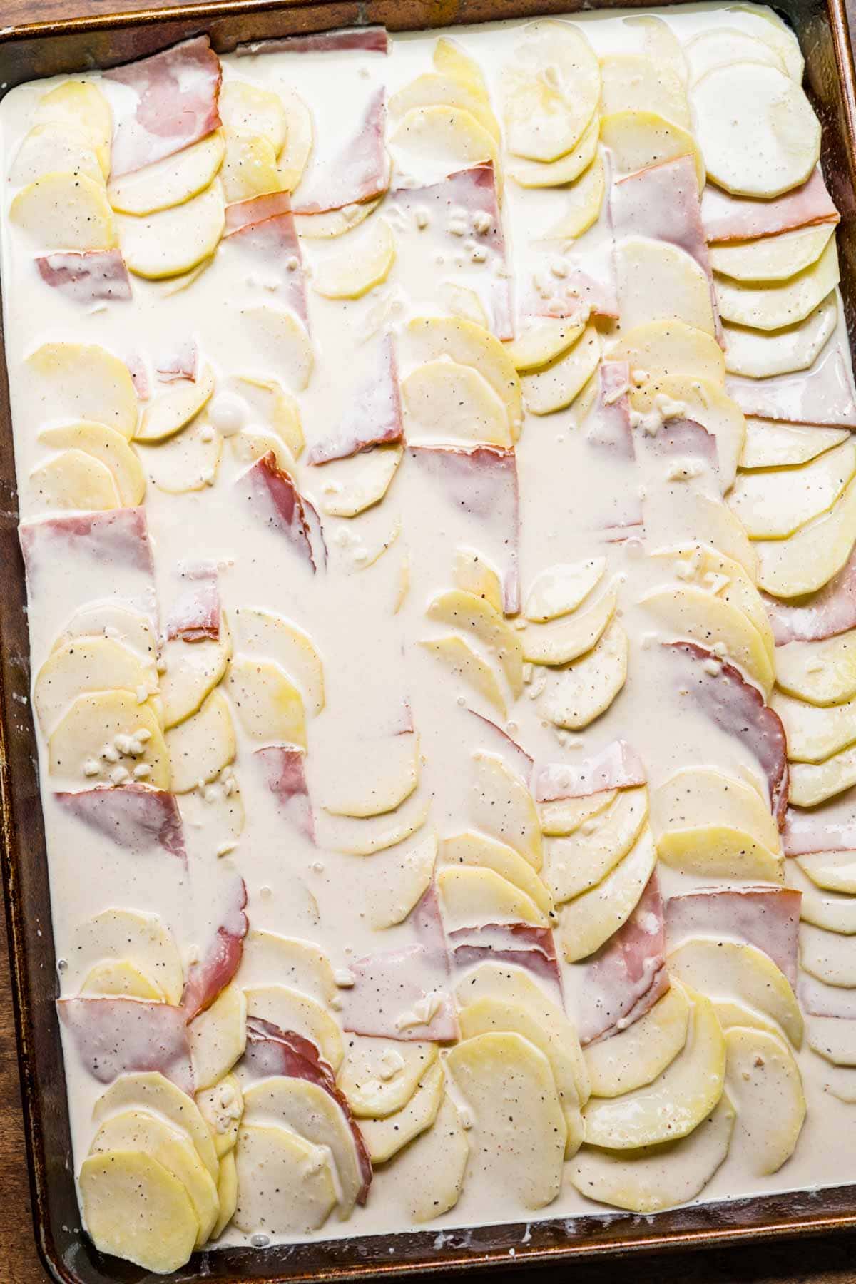 Sheet Pan Ham and Swiss Scalloped Potatoes layered on sheet pan unbaked