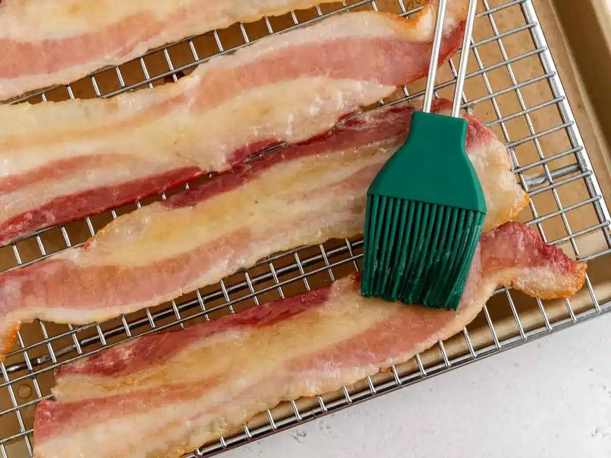 Thin slices of cured pork being brushed with syrup.