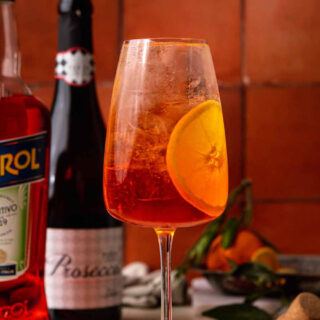 Refreshing cocktail in tall wine glass with orange garnish.
