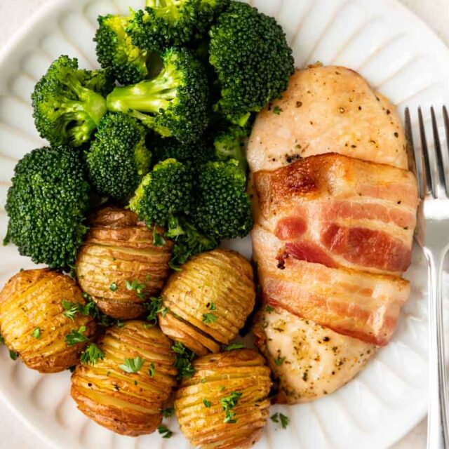 Bacon wrapped chicken plated with broccoli and small potatoes