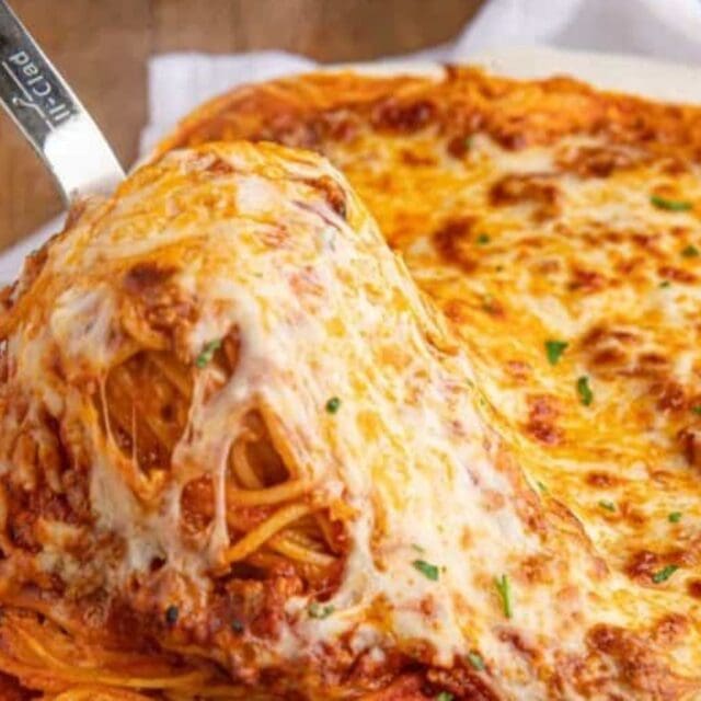 Serving pasta from a white baking dish.