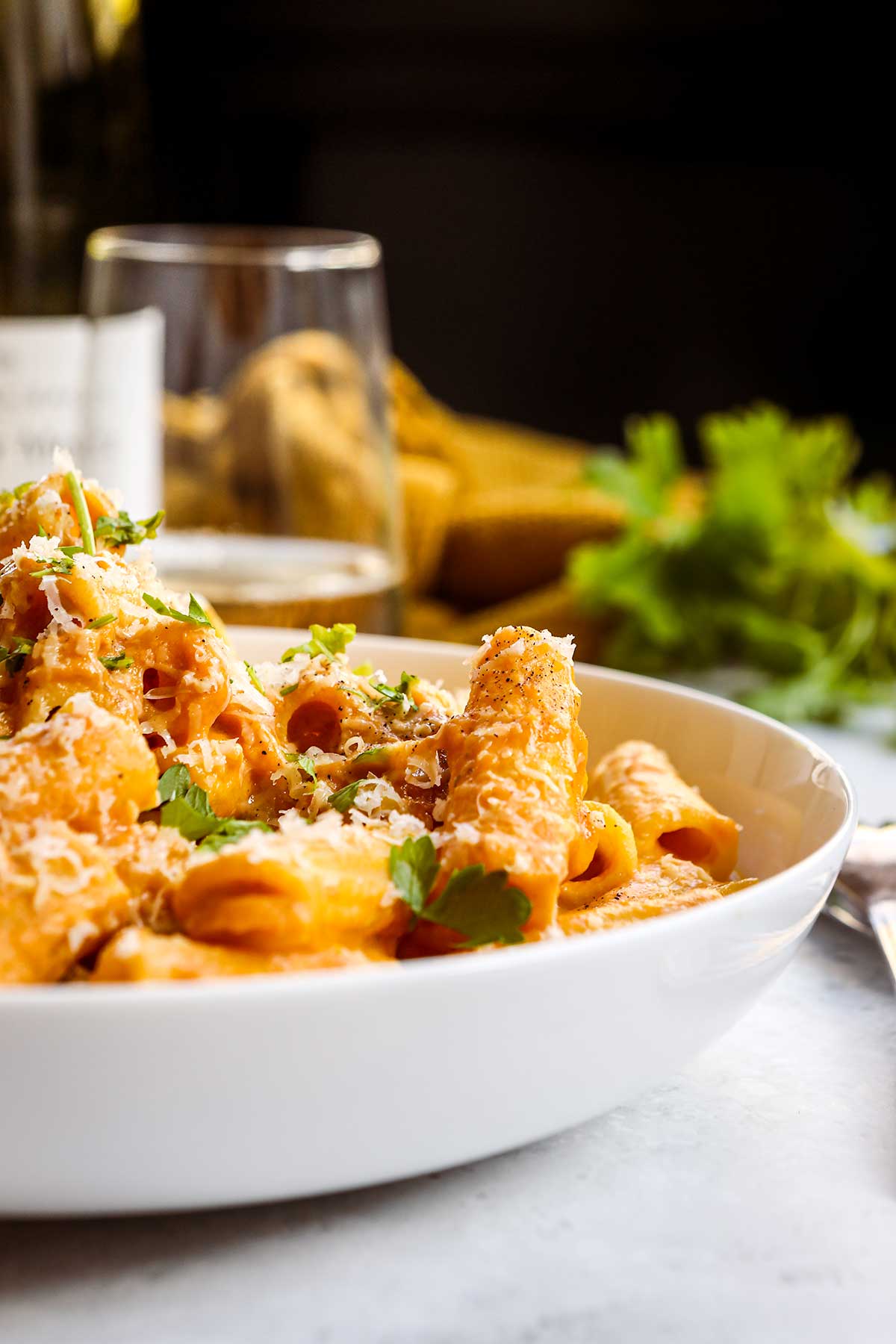 Creamy Pumpkin Pasta in bowl topped with Parmesan cheese and parsley side view with bottle of wine