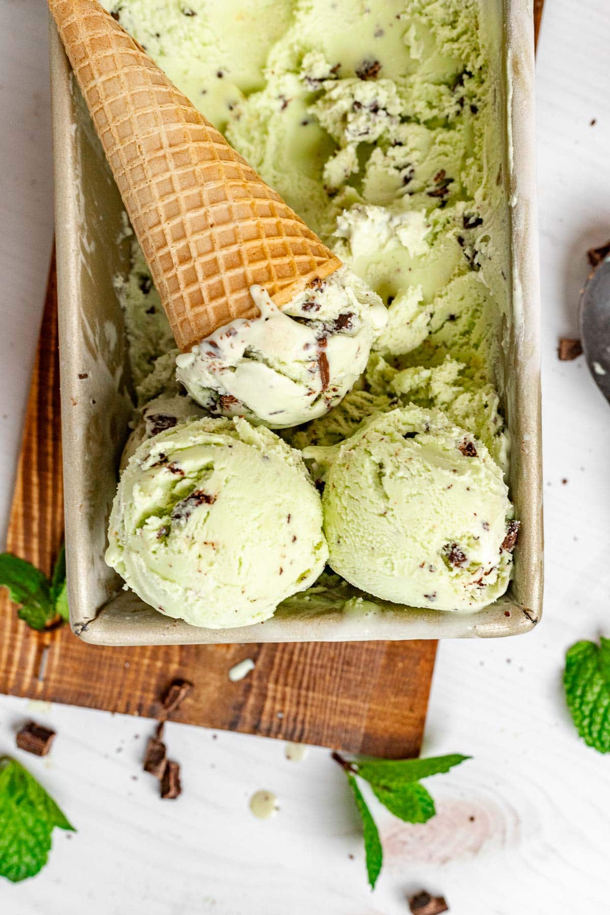 Mint Chocolate Chip Ice Cream in pan finished with scoops and cone on top