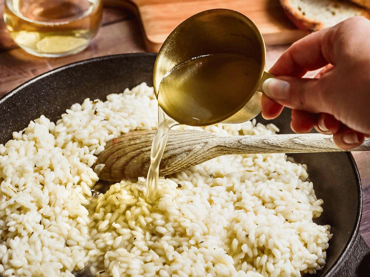 pouring broth into rice in pan