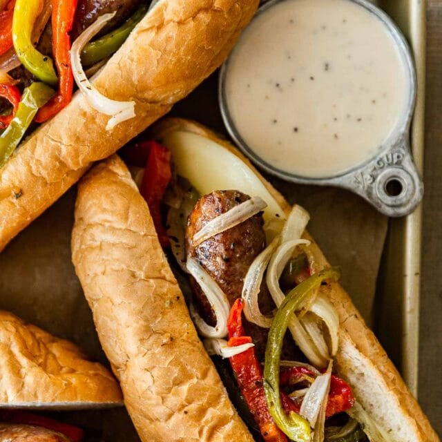 Sheet Pan Sausage and Peppers in hoagie rolls with dressing on side
