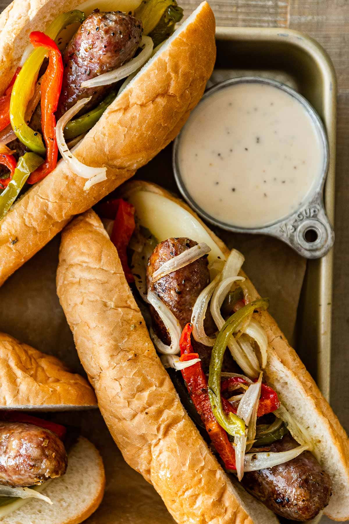 Sheet Pan Sausage and Peppers in hoagie rolls with dressing on side