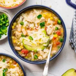 Black serving bowl of white bean chili with garnish and silver spoon.