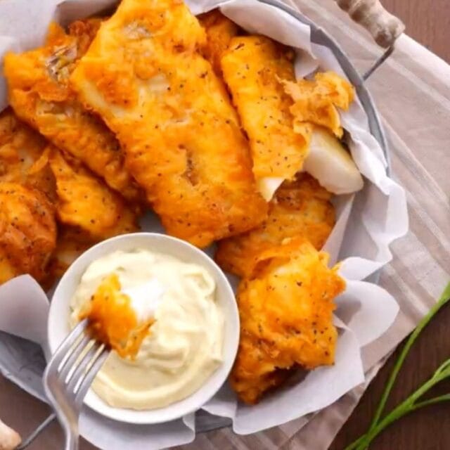 Battered Fish basket of fried fish pieces with a small bowl of tartar sauce. Fork with bite over tartar sauce. 1x1