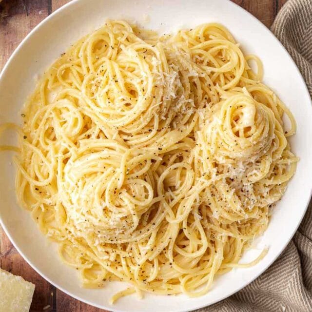 Plate of spaghetti with Romano, Parmesan, and black pepper.