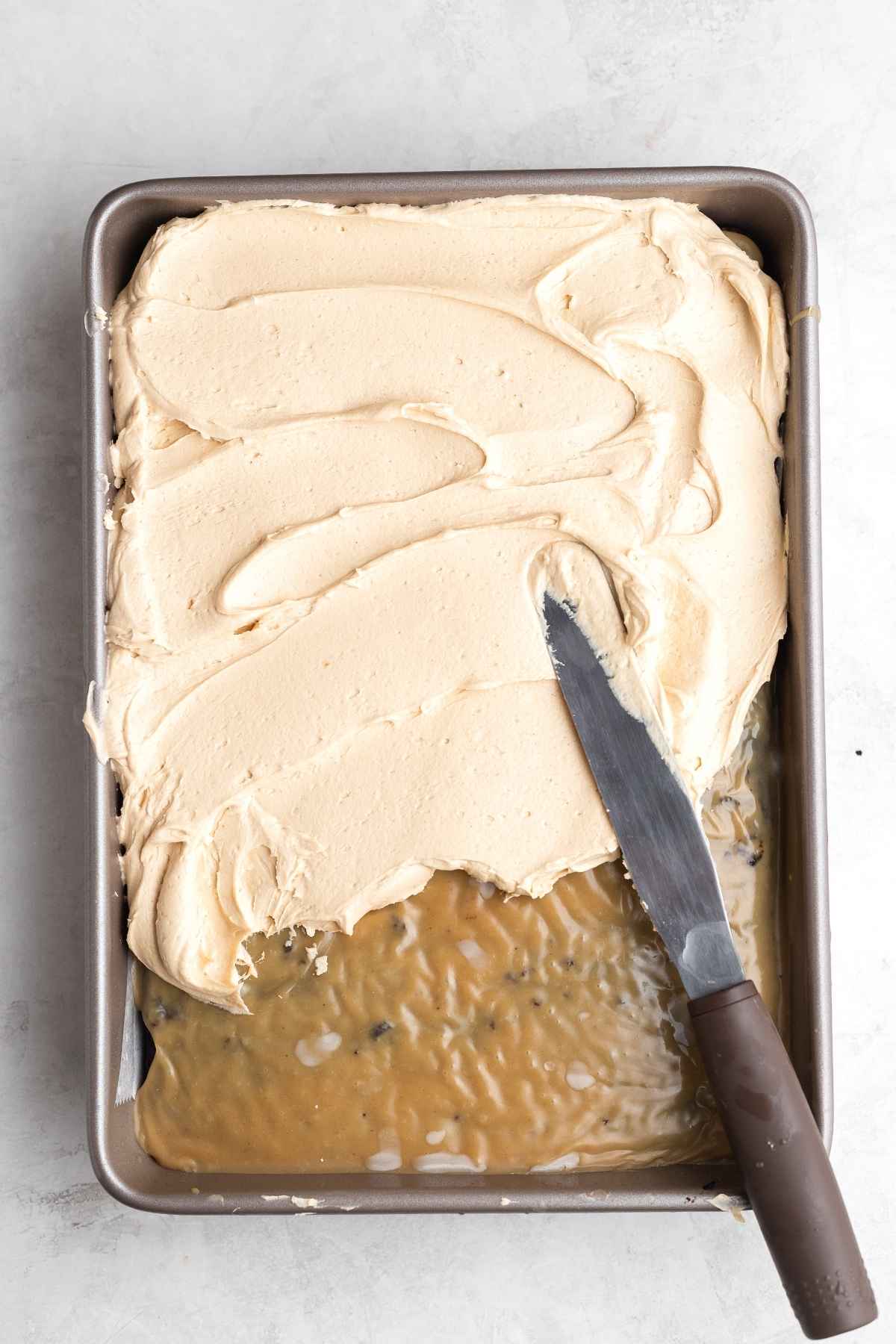 Peanut Butter Chocolate Poke Cake in pan adding frosting