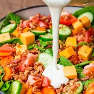 green salad with dressing being poured on it