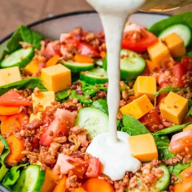 green salad with dressing being poured on it