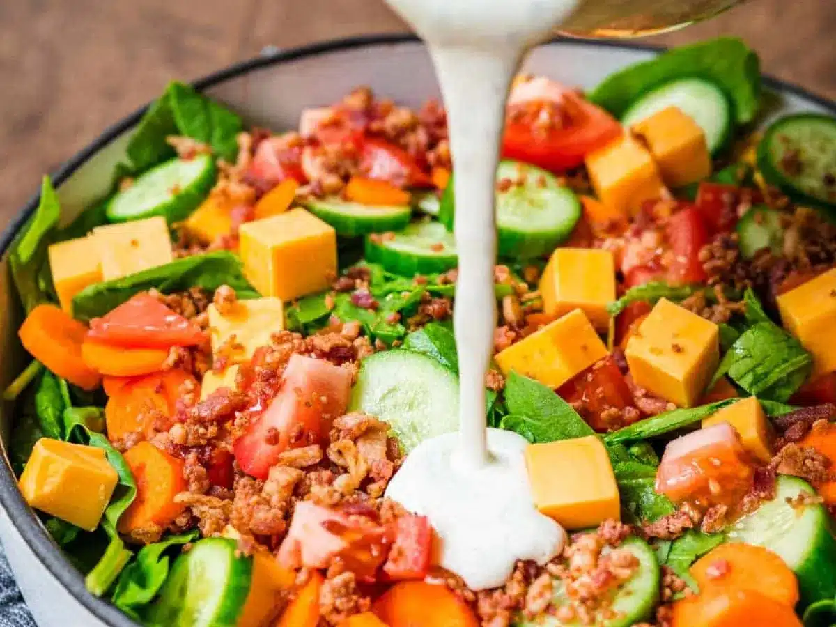 green salad with dressing being poured on it 