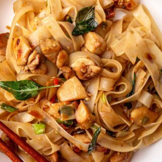 Wide rice noodle dish with chicken on plate.