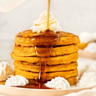 Pumpkin Pancakes stack of six pancakes with whipped cream and syrup being poured