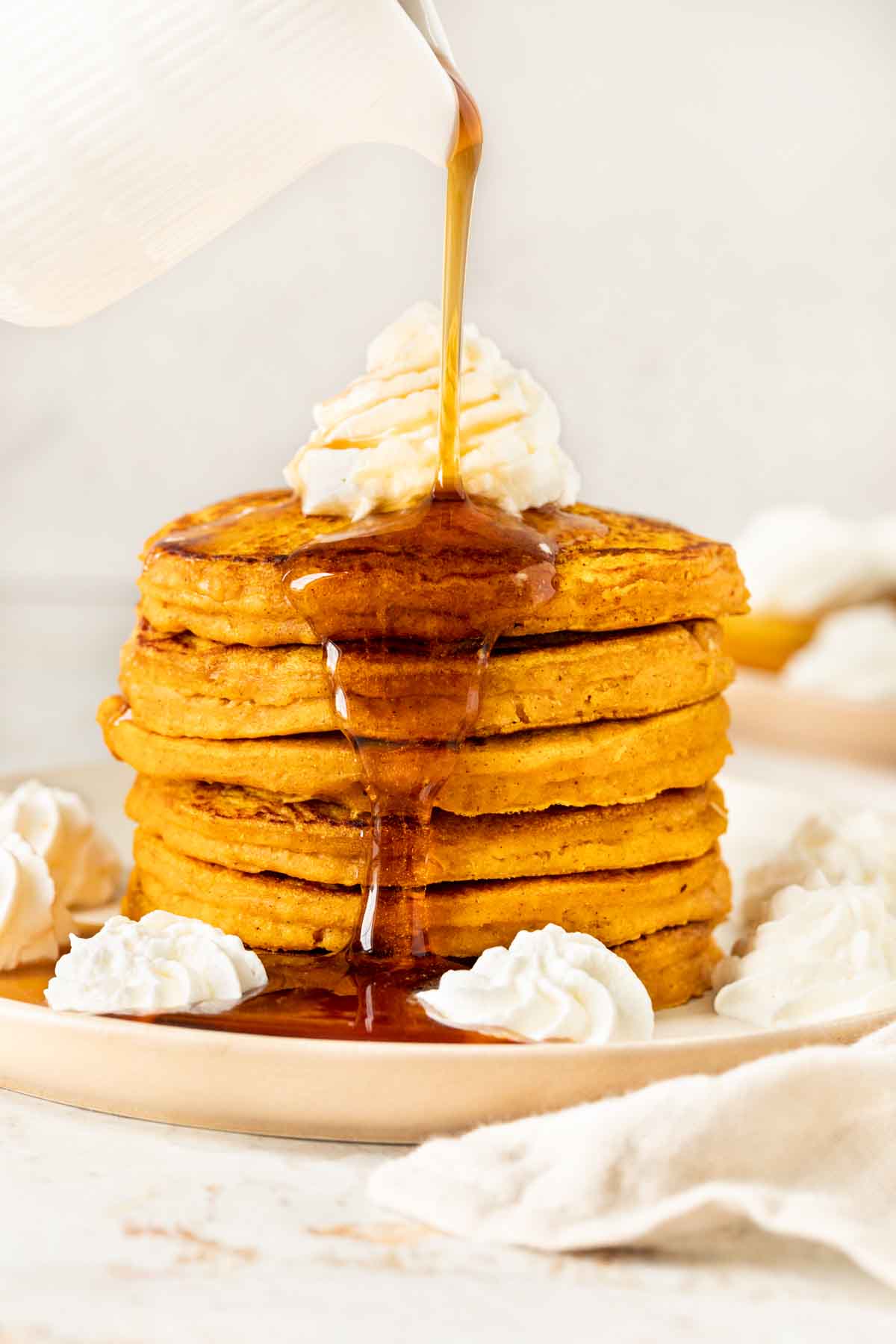 Pumpkin Pancakes stack of six pancakes with whipped cream and syrup being poured