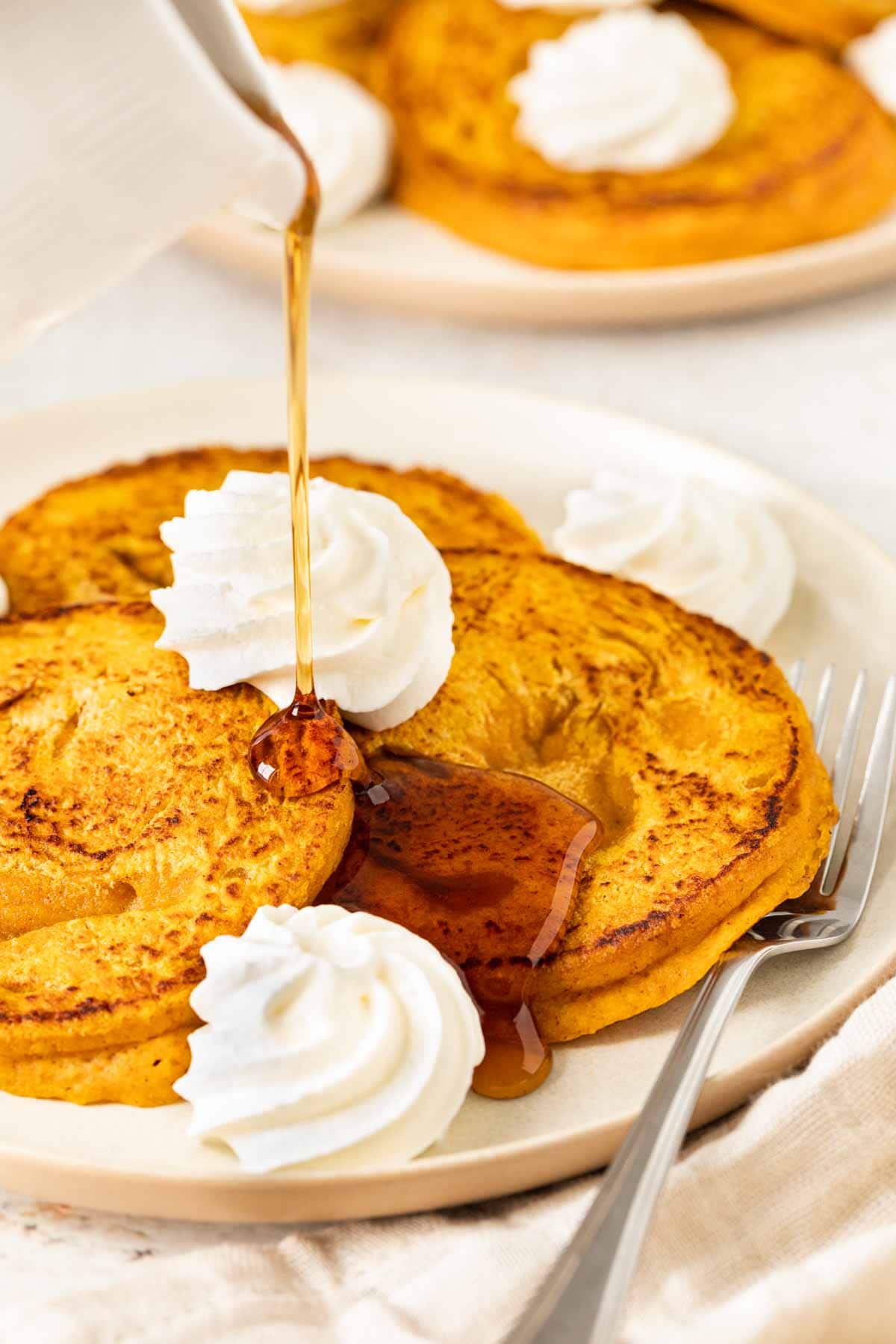 Pumpkin Pancakes three pancakes on plate with whipped cream and syrup