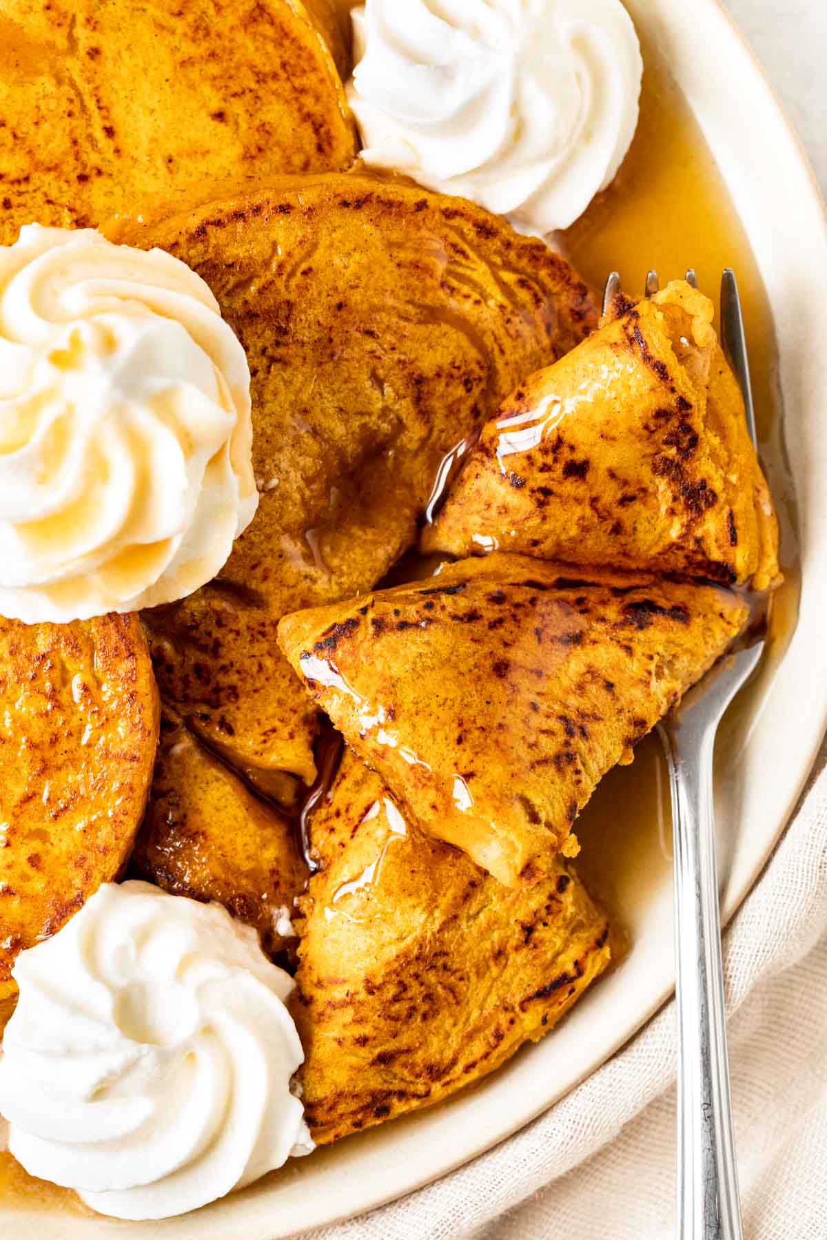 Pumpkin Pancakes pancakes on plate with bite cut topped with whipped cream and syrup
