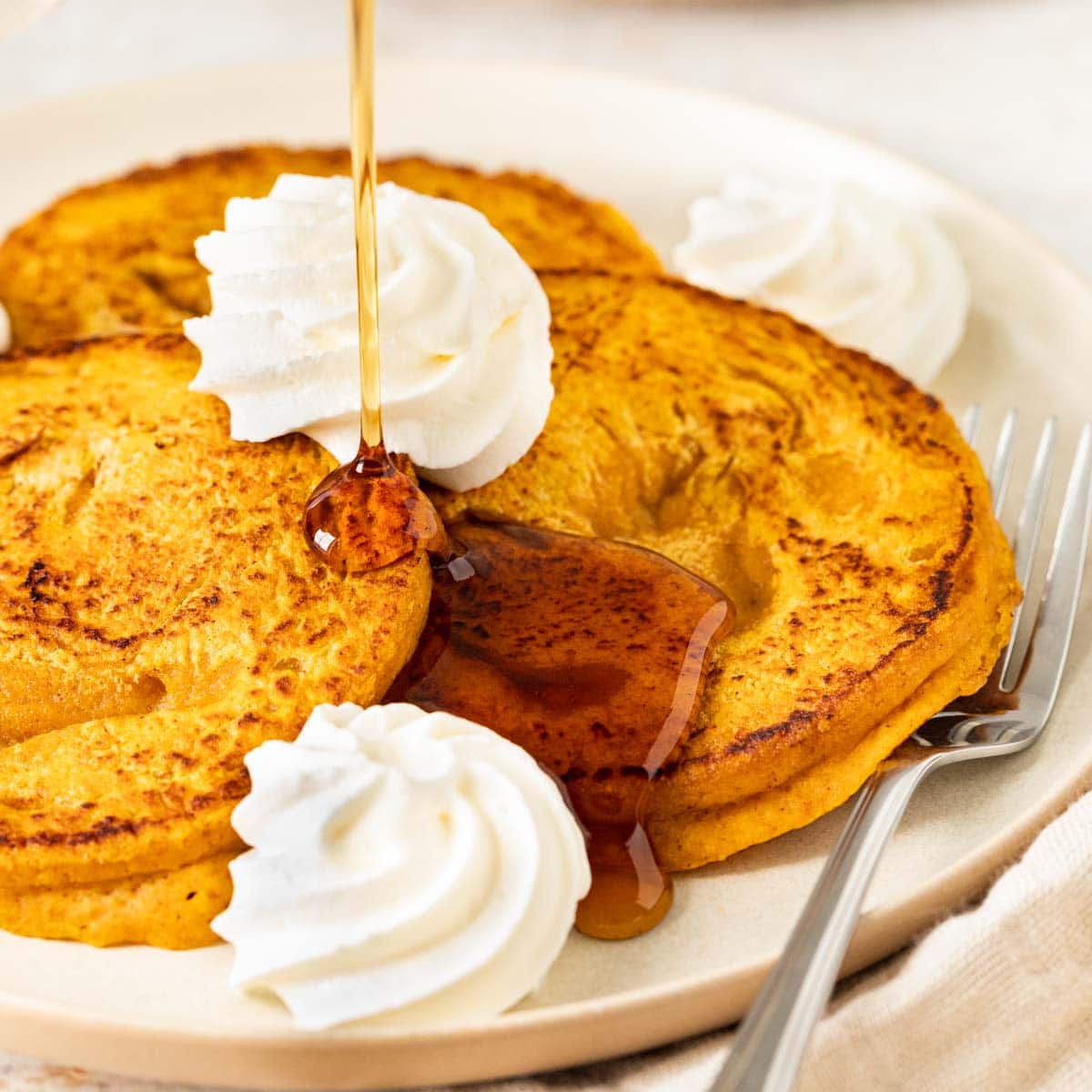 Pumpkin Pancakes three pancakes on plate with whipped cream and syrup