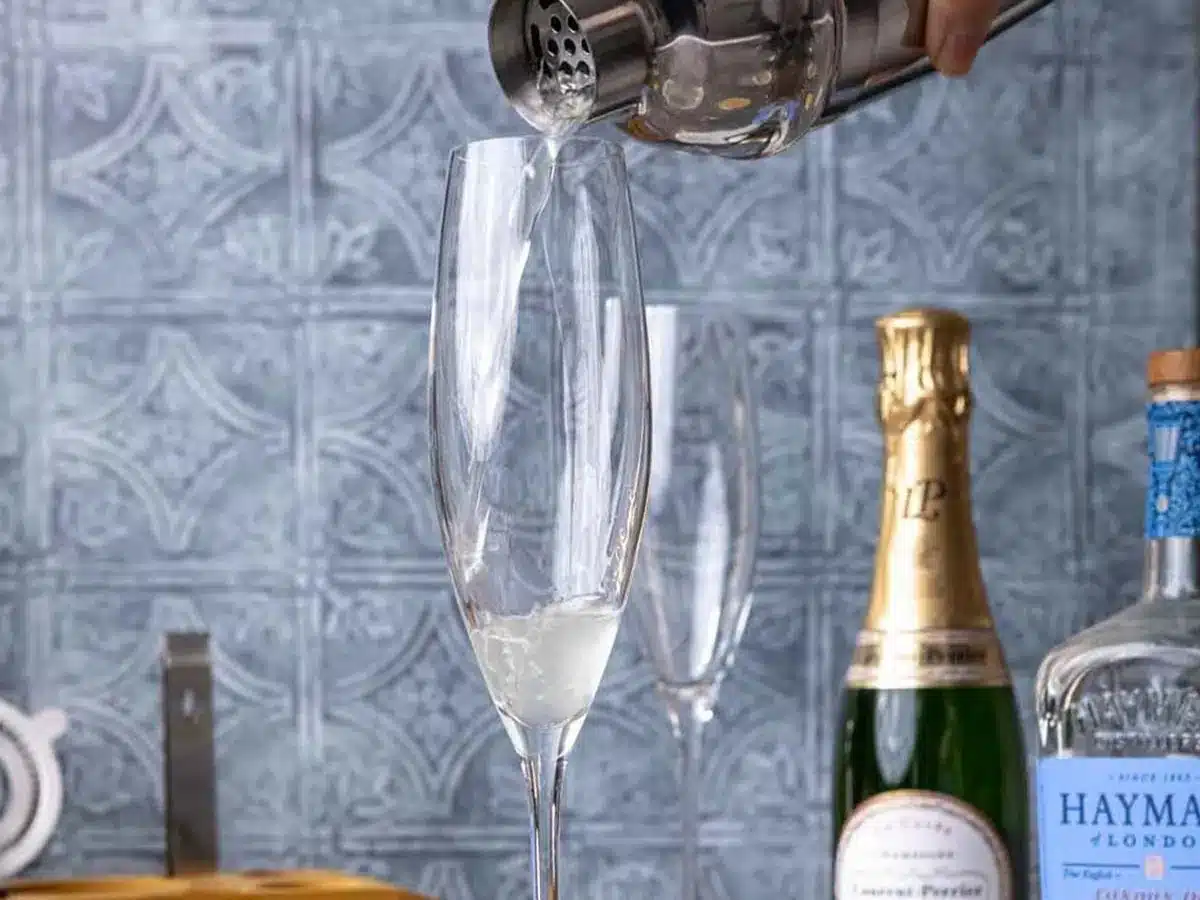 Gin, lemon juice, and simple syrup being added to flute.