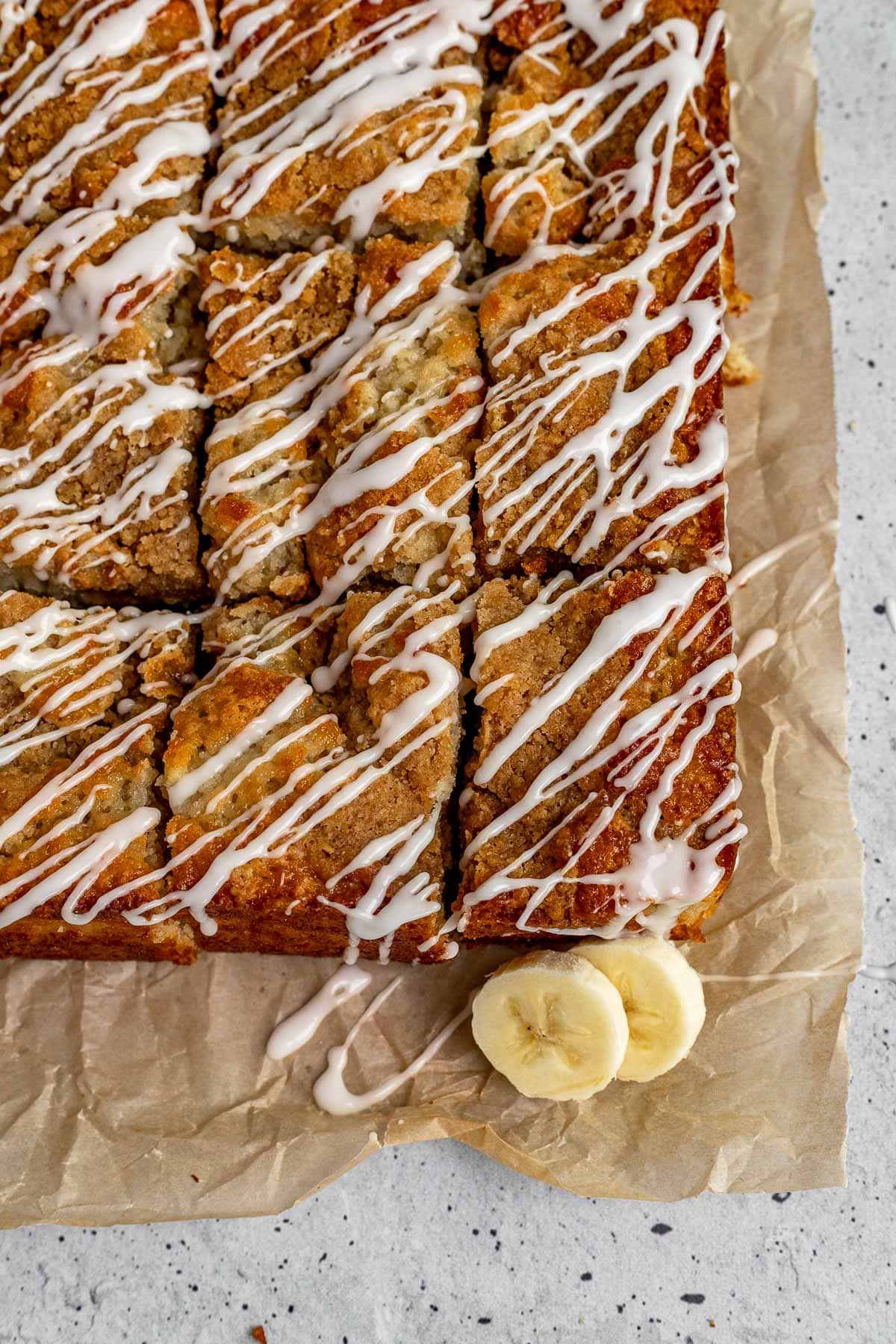 Banana Bread Crumb Cake sliced on cutting board with icing drizzle