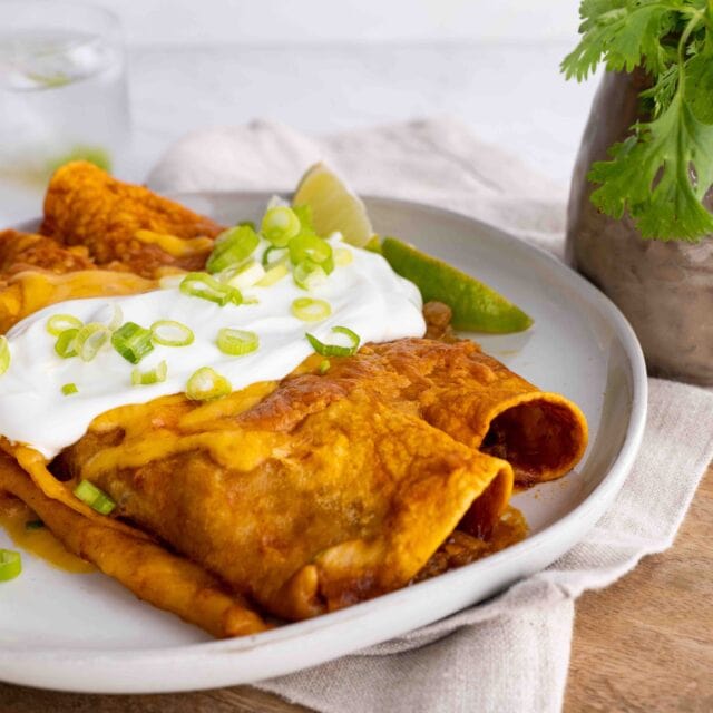 side view Beef enchiladas on plate topped with sour cream