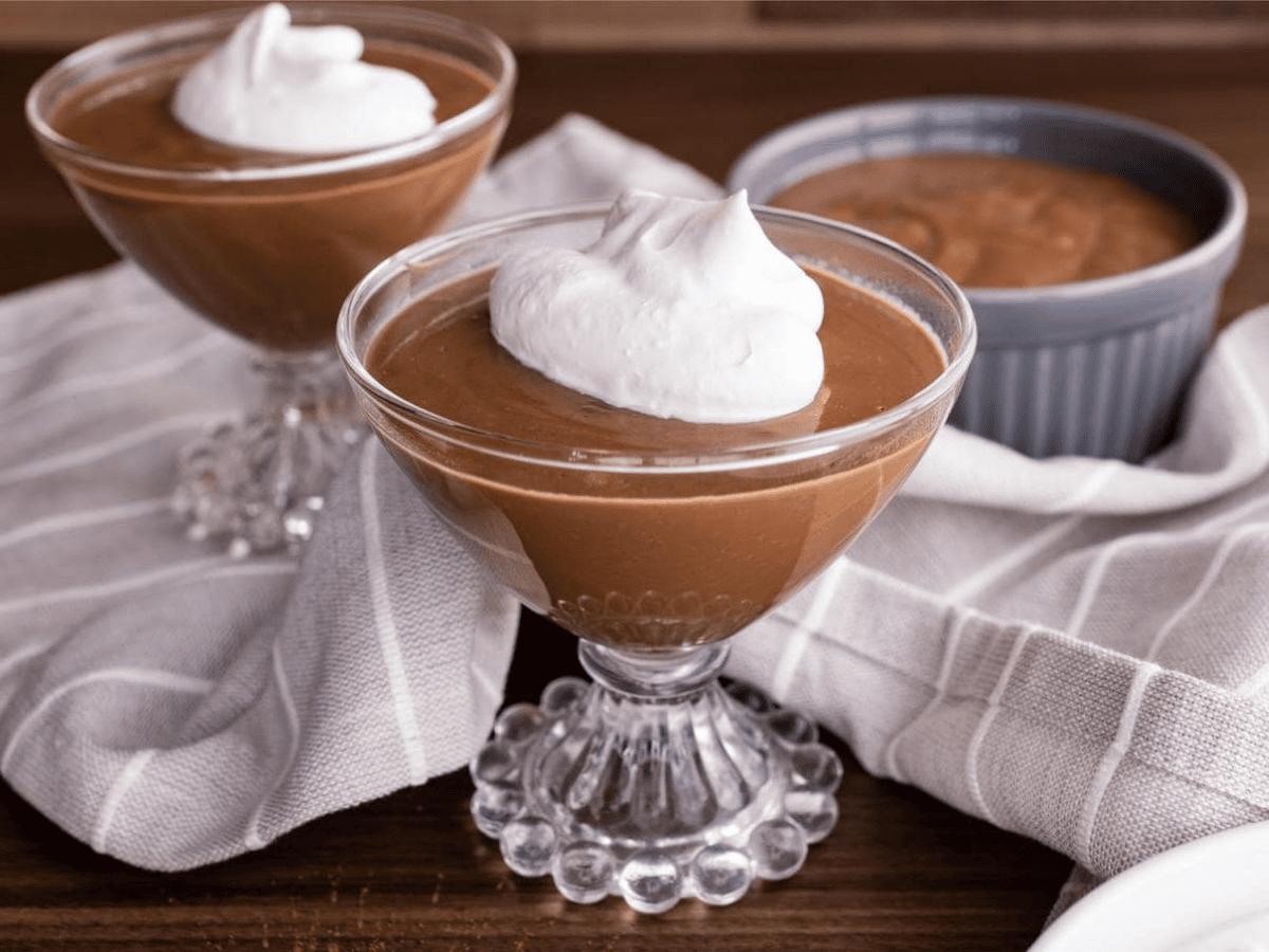 pudding being served in fancy glasses topped with whipped cream 